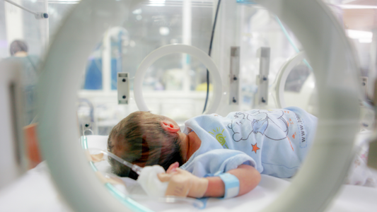 Premature infant in incubator in NICU with blue onesie