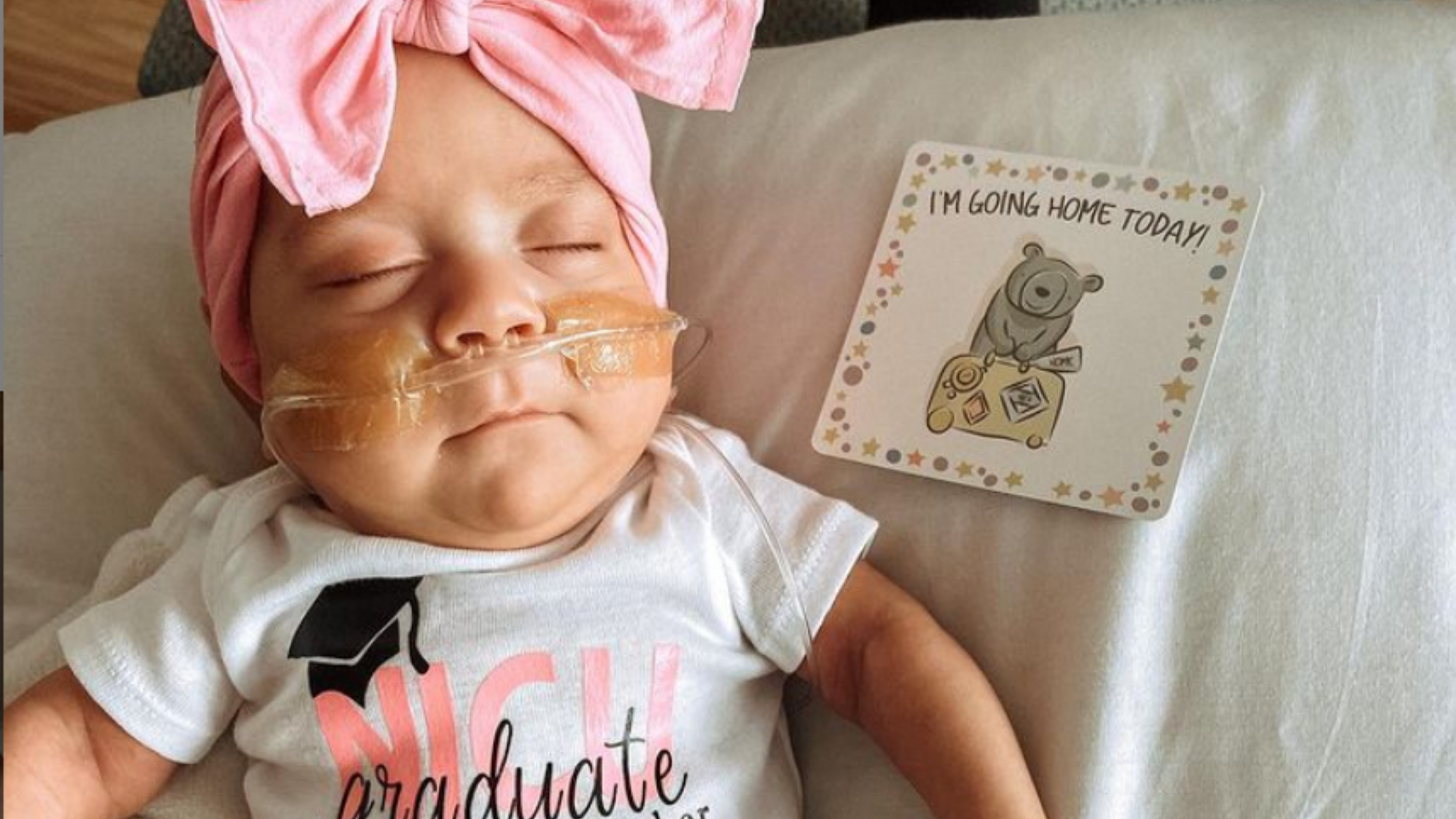 Preemie baby with oxygen in NICU next to "Im going home" milestone card